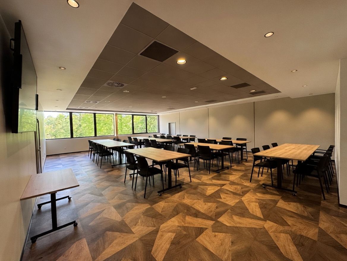 Le Salon Orangerie aménagé pour un séminaire, avec ses tables en bois et ses baies vitrées sur le parc