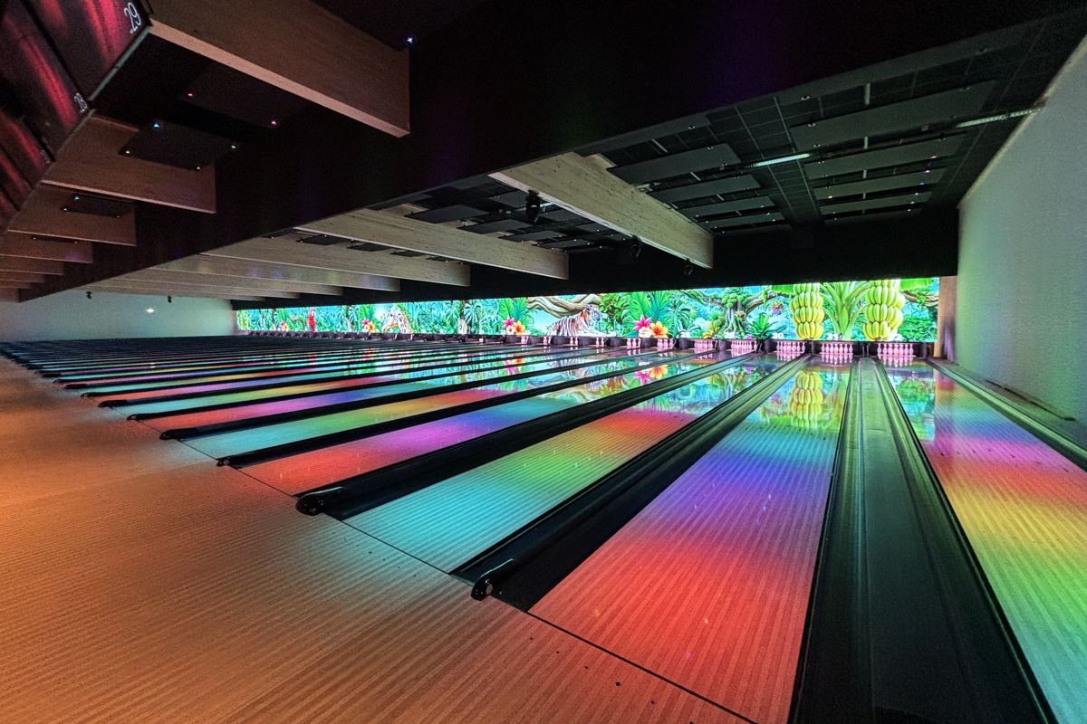 Les pistes de BAD BOWL Strasbourg éclairées en couleurs, devant un grand mur lumineux de jungle
